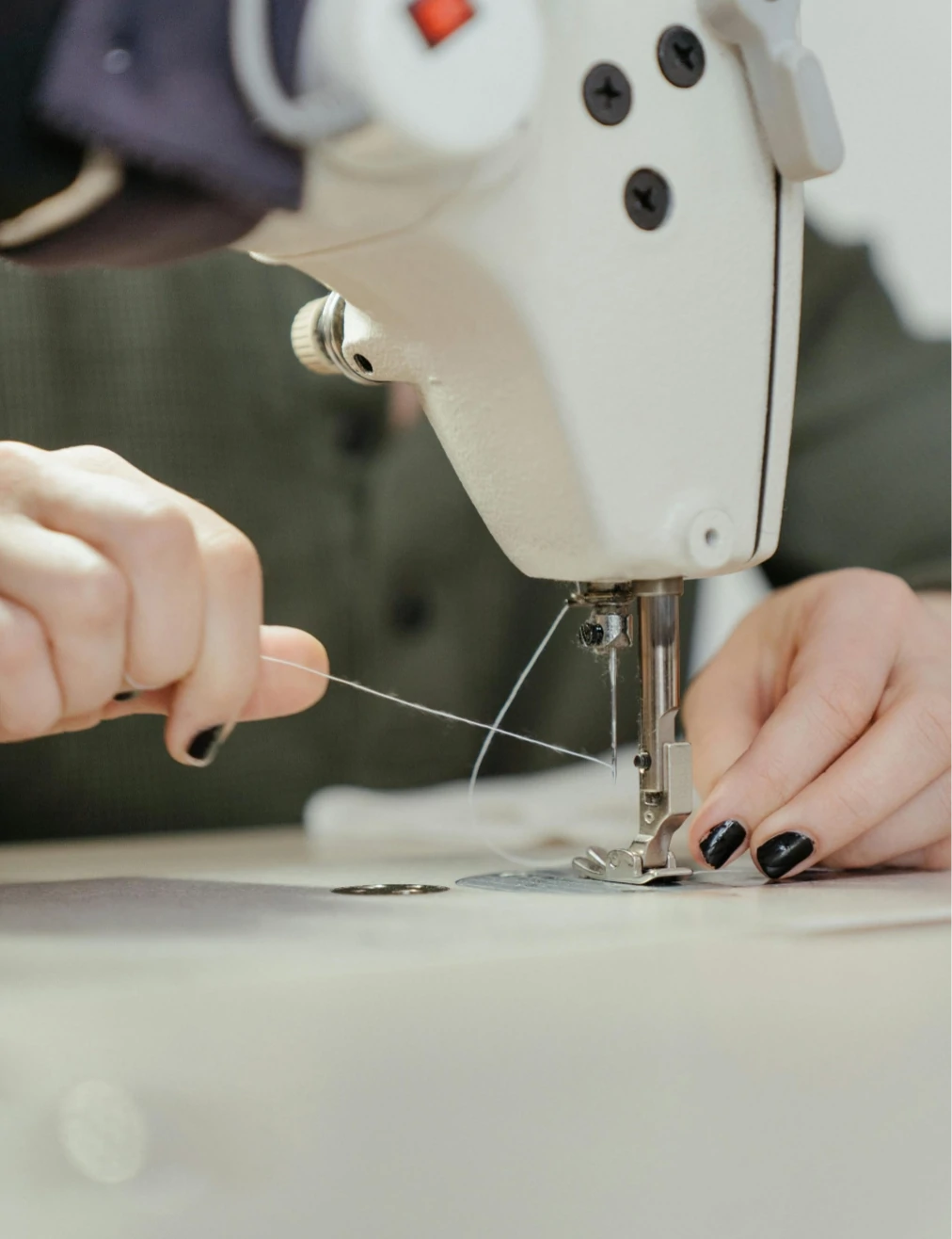 Detalle de mujer cortando con sus manos un hilo que está sujeto a la máquina de coser@2x