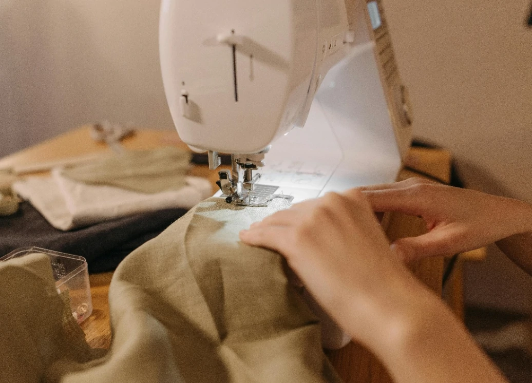 detalle de manos con tela cosiendo en máquina de coser@2x